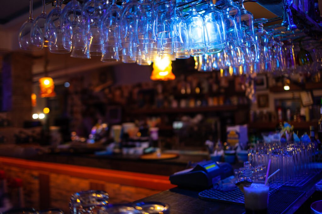 In the bar. Counter with served drink, clean glasses on the counter and over it. View in dim light